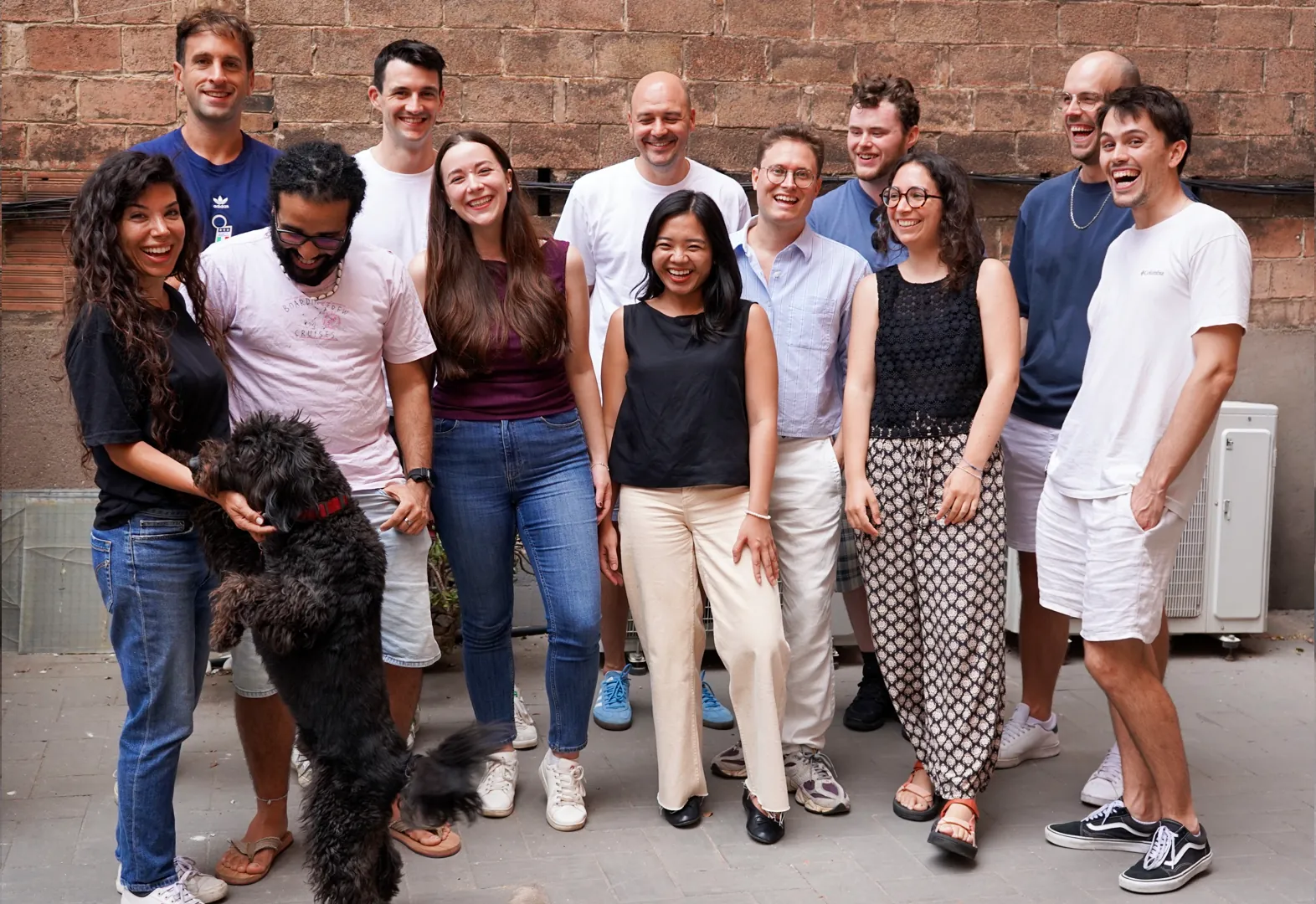 The Rowmesh team together in a courtyard, with a black dog jumping up to greet them